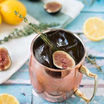 A closeup of a mule cocktail in a copper mug with figs and fresh thyme.