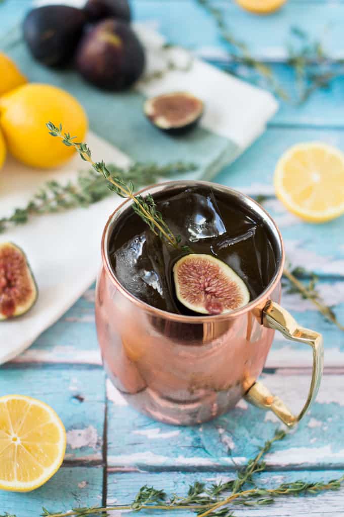 A closeup of a mule cocktail in a copper mug with figs and fresh thyme.