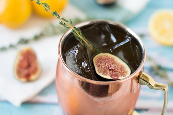 A closeup of a mule cocktail in a copper mug with figs and fresh thyme.