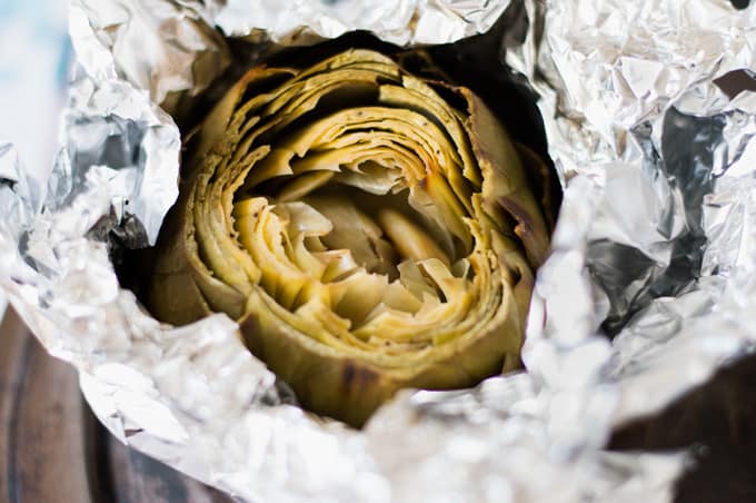 A closeup of a roasted artichoke in tin foil.