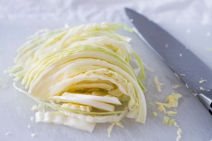 Sliced cabbage on a cutting board with a chef\'s knife.