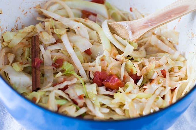 A close up of shredded cabbage and tomatoes in a dutch oven.