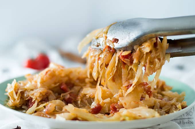 A closeup of tongs picking up some shredded cabbage from a plate.