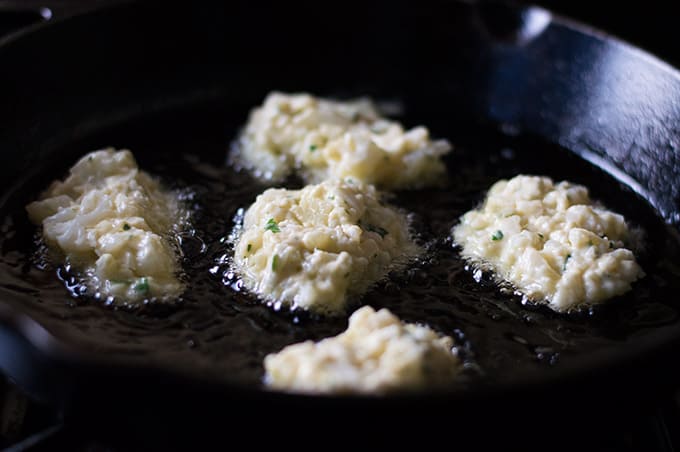 Cauliflower fritters frying in a pan of oil.