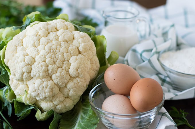 Cauliflower, a bowl of eggs, and milk on a tabletop.