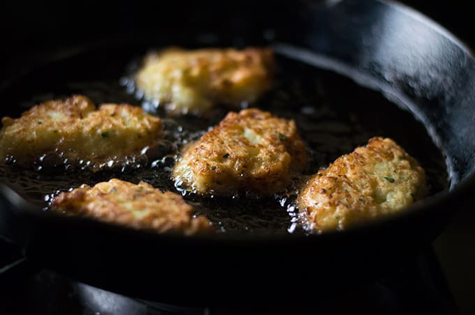 A closeup of cauliflower fritters frying in a pan of oil.