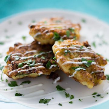 Closeup of cauliflower fritters on a plate drizzled with yogurt sauce.