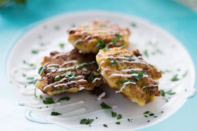 Closeup of cauliflower fritters on a plate drizzled with yogurt sauce.