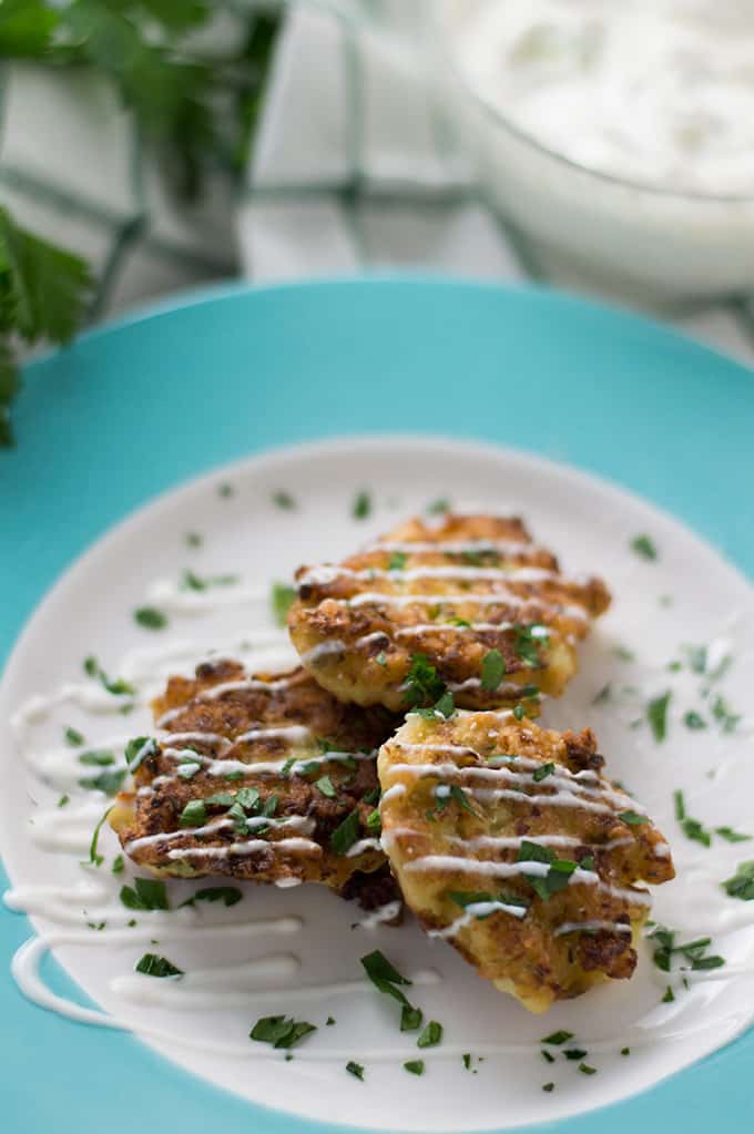 A plate of cauliflower fritters drizzled with yogurt sauce.