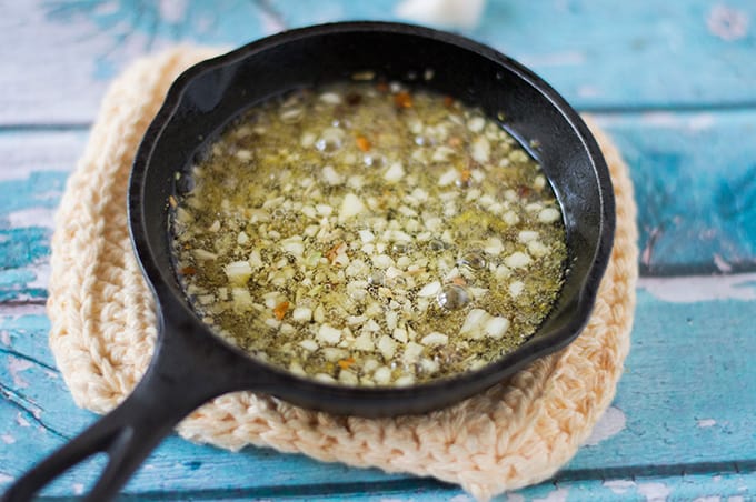 A small skillet of garlic, spices, and oil.