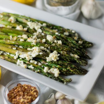 A plate of roasted asparagus topped with feta cheese.