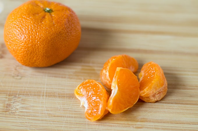 Peeled orange pieces and a whole orange on a cutting board.