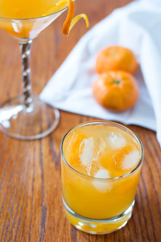 An orange drink in assorted cocktail glasses with oranges in the background.