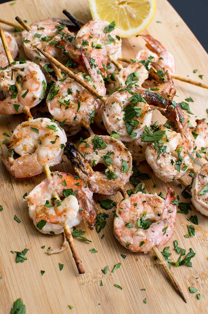 Close up of grilled skewered shrimp on a cutting board.