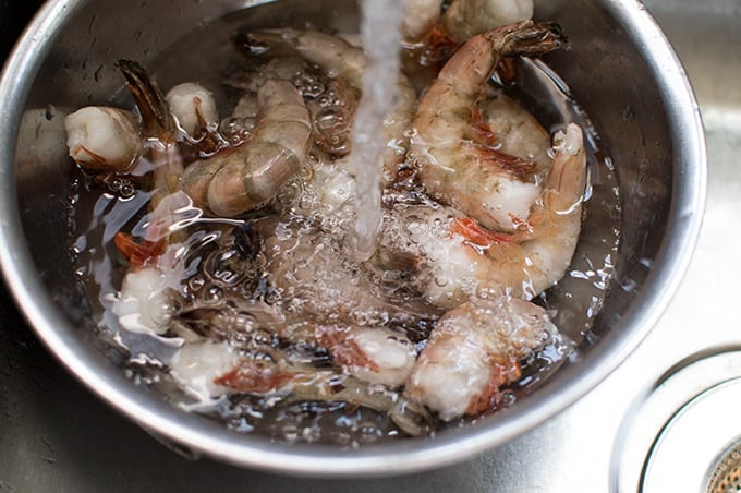 Closeup of frozen shrimp defrosting in a bowl under running water from a sink.