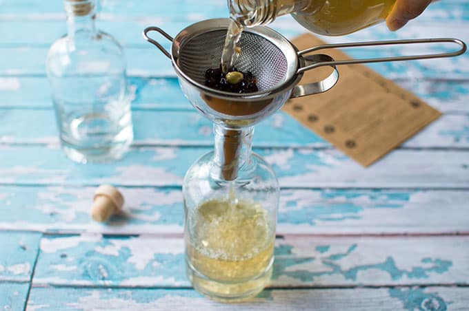 Liquid being poured into a glass bottle through a fine mesh sieve and funnel.