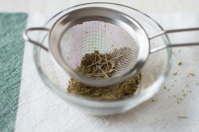 Spices being sifted through a fine mesh strainer into a small bowl.