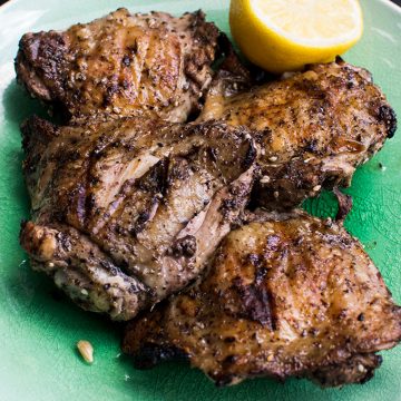 Close up of grilled chicken on a plate with half a lemon.