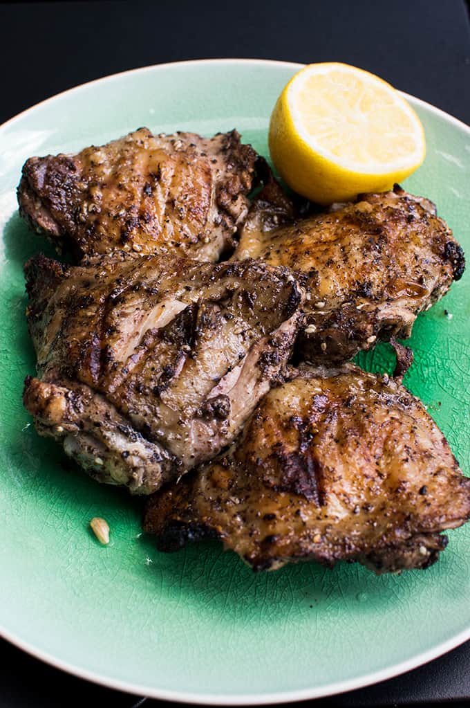 Close up of grilled chicken on a plate with half a lemon.