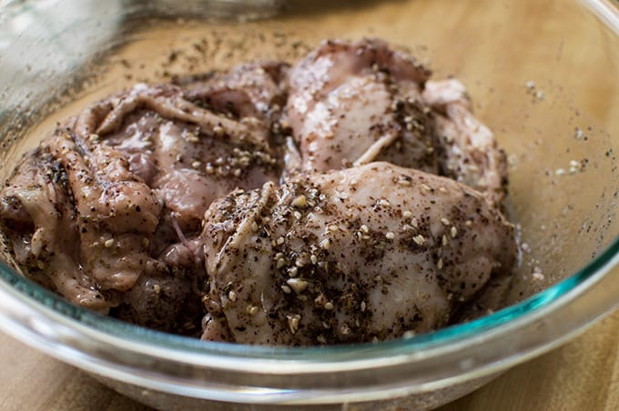 Close up of seasoned raw chicken in a glass bowl.