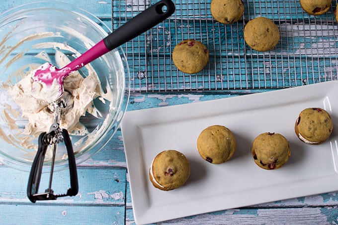 A bowl of dulce de leche filling, a baker\'s rack of miniature cakes, and a plate of prepared pumpkin whoopie pies.