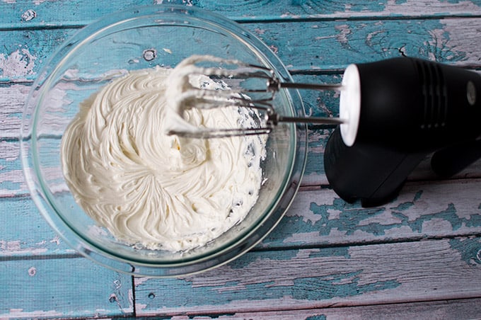 Whipped icing and a hand mixer on a table.