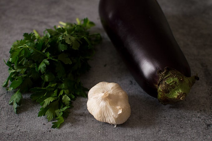 Parsley, a bulb of garlic, and an eggplant on a table.