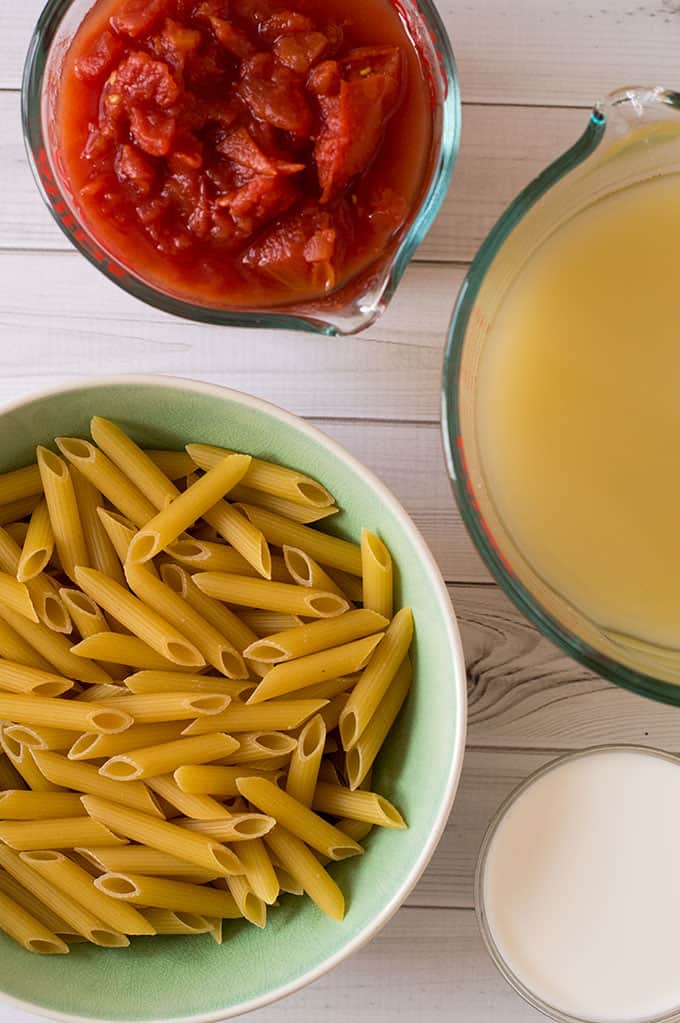 Bowls of tomatoes, chicken stock, raw penne pasta, and cream.