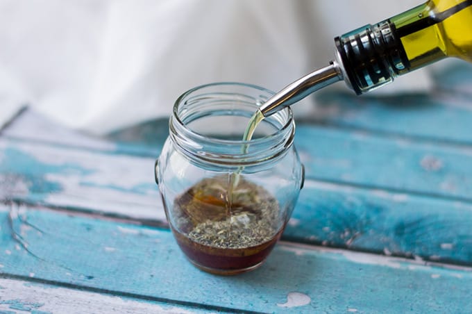 Olive oil being poured into a glass jar.