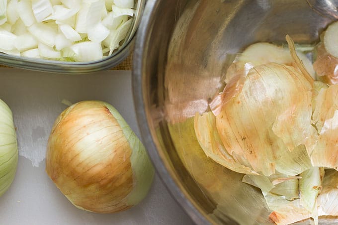 A bowl of onion scraps, bowl of chopped onions, and a whole onion on a cutting board.