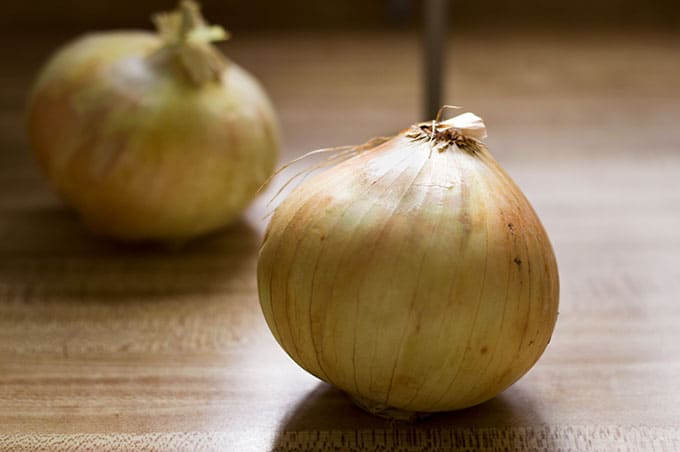 Close up of whole onions on a cutting board.