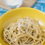 A bowl of cacio e pepe spaghetti with grated cheese in the background.