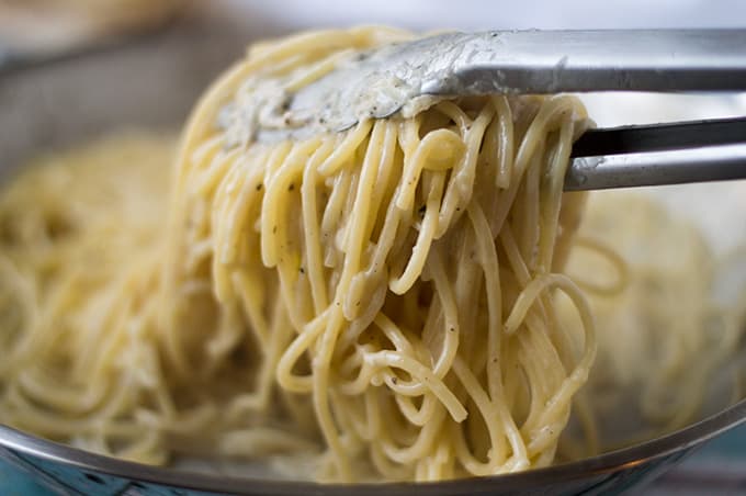 Close up of tongs holding up spaghetti.