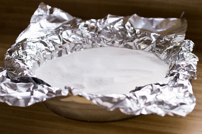 A pie pan lined with aluminum foil and filled with sugar.
