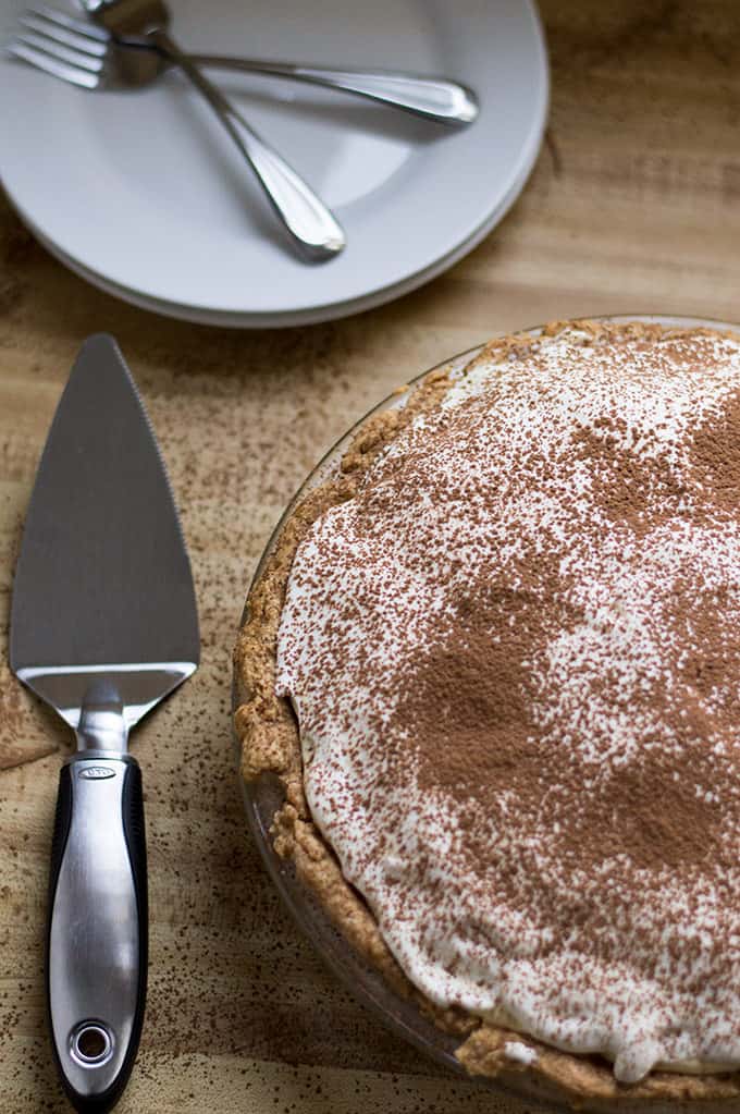 Whole tiramisu pie with a pie server and plates in the background.