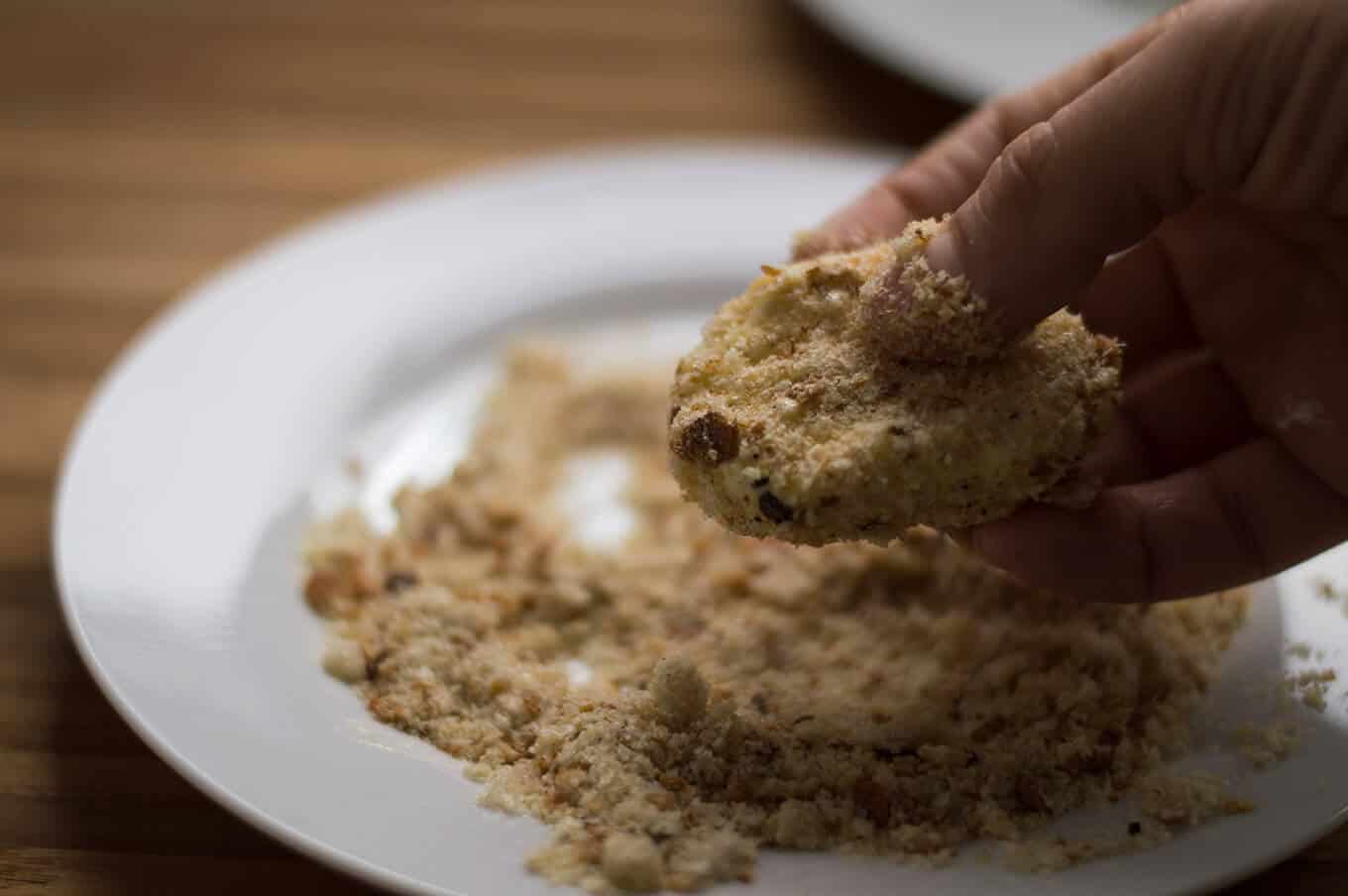 A hand holding a breaded piece of goat cheese.