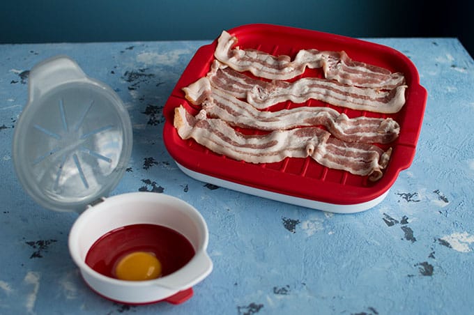 Microwavable cooking containers with raw bacon and egg.