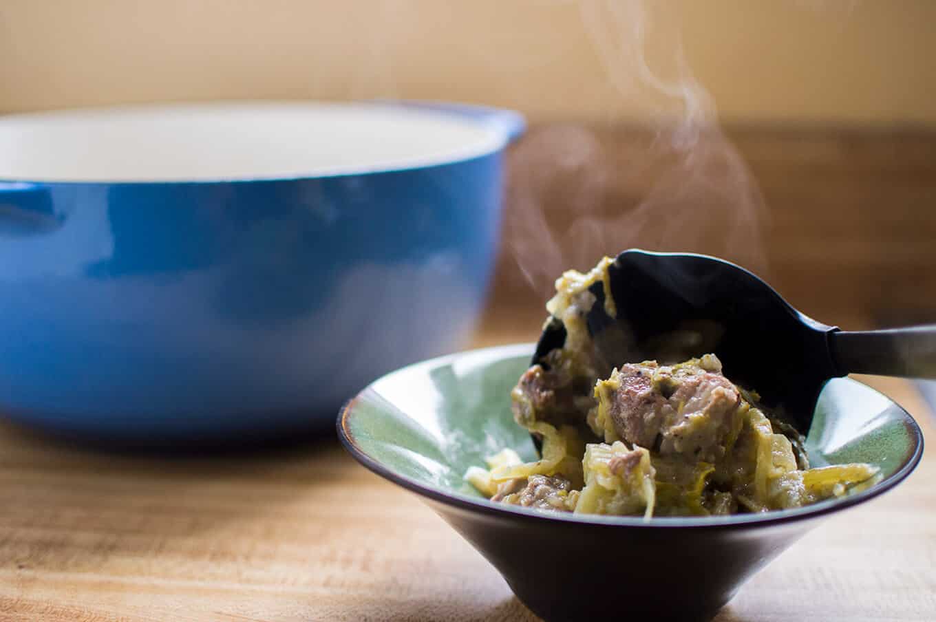 A ladle pouring pork and celery stew into a bowl.