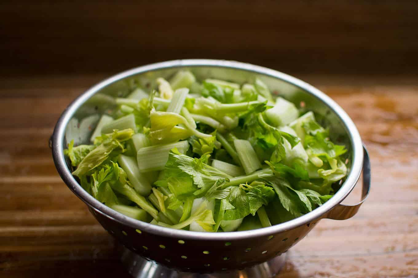 A colander filled with chopped celery ribs and leaves.