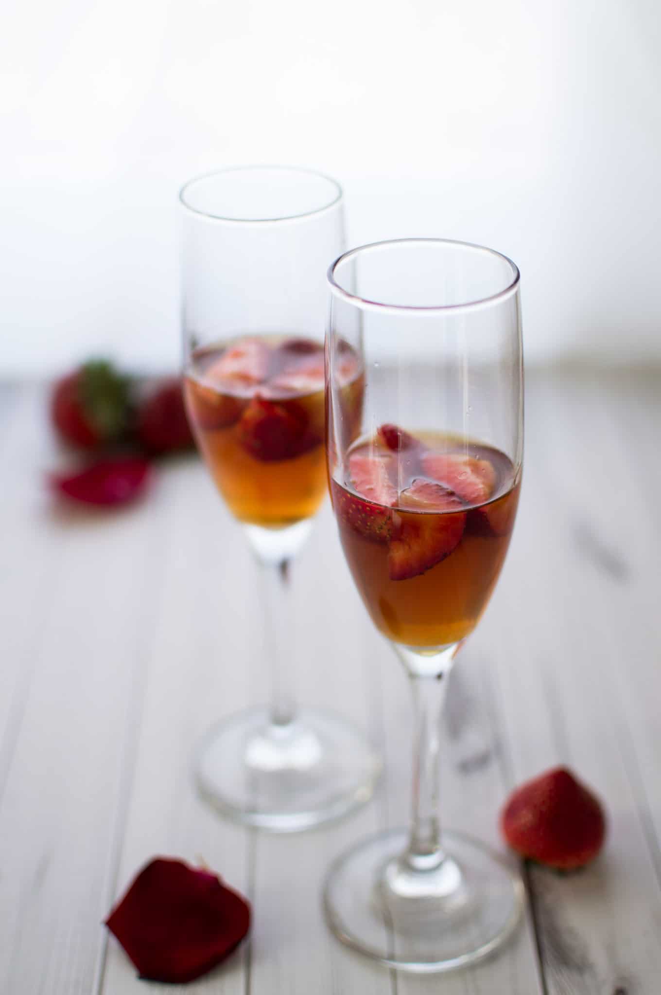 Close up of champagne glasses half-filled with strawberries and fig vodka.