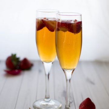 Two champagne glasses filled with cocktails and fresh strawberries.