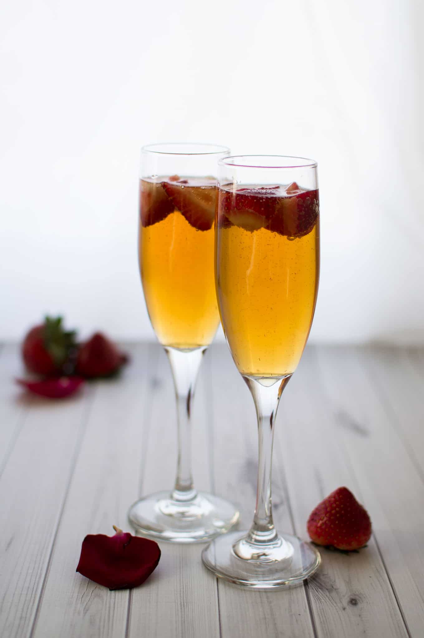 Two champagne glasses filled with cocktails and fresh strawberries.