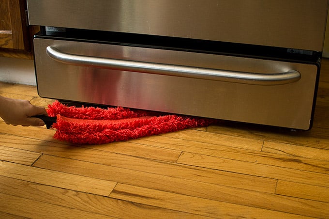 A duster cleaning beneath an oven.