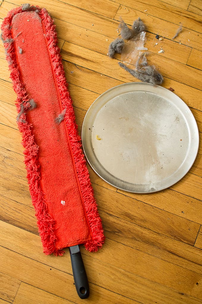 A duster on the floor with clumps of dust and a pizza pan.