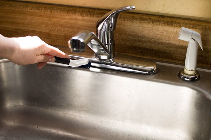 A kitchen faucet being cleaned with a scrub brush.