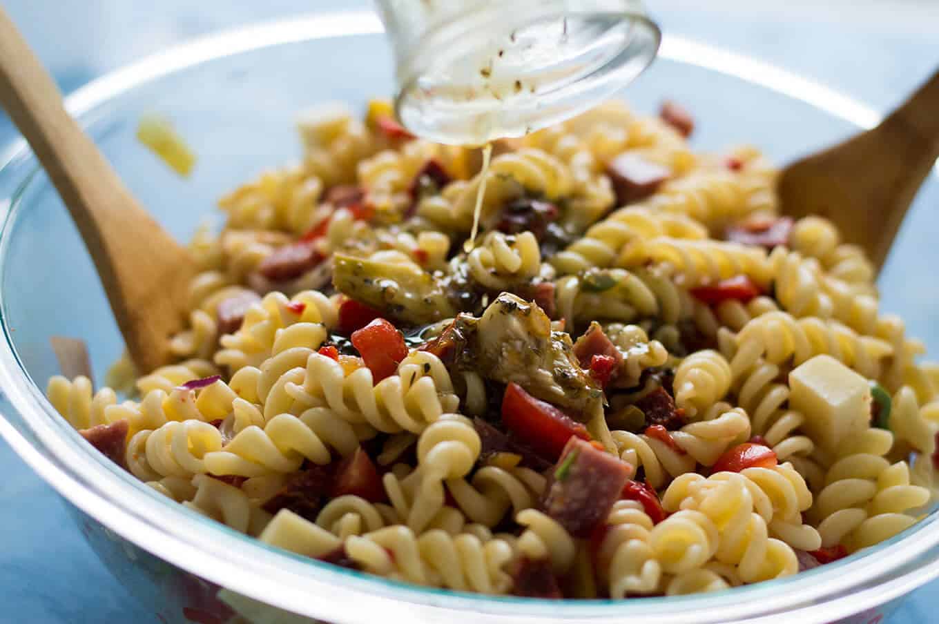 Dressing being poured over a bowl of pasta salad.