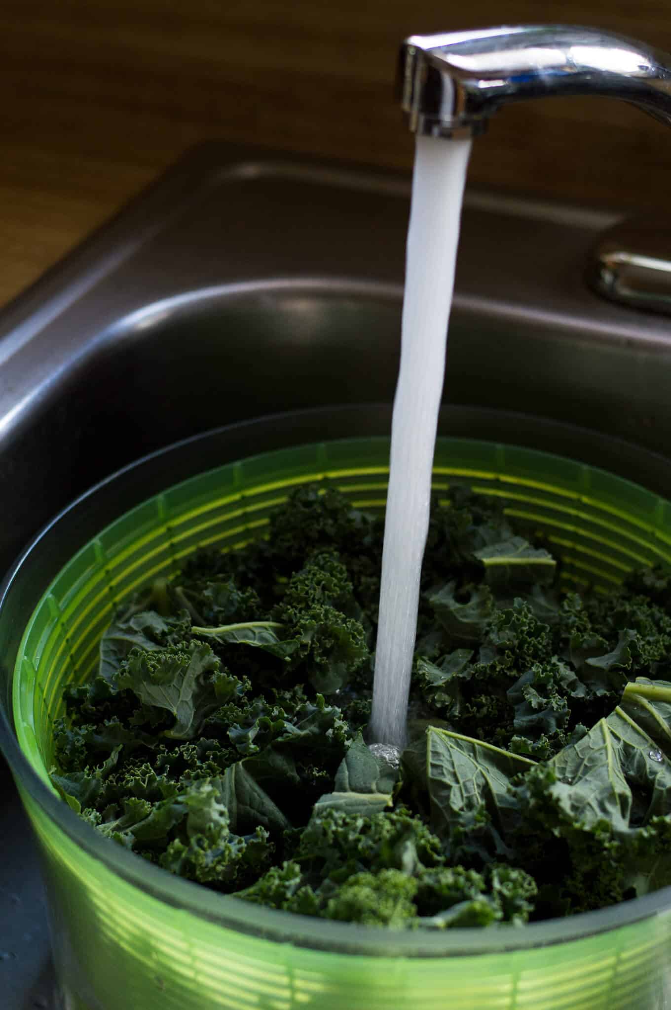 Kale in a salad spinner under a running faucet.