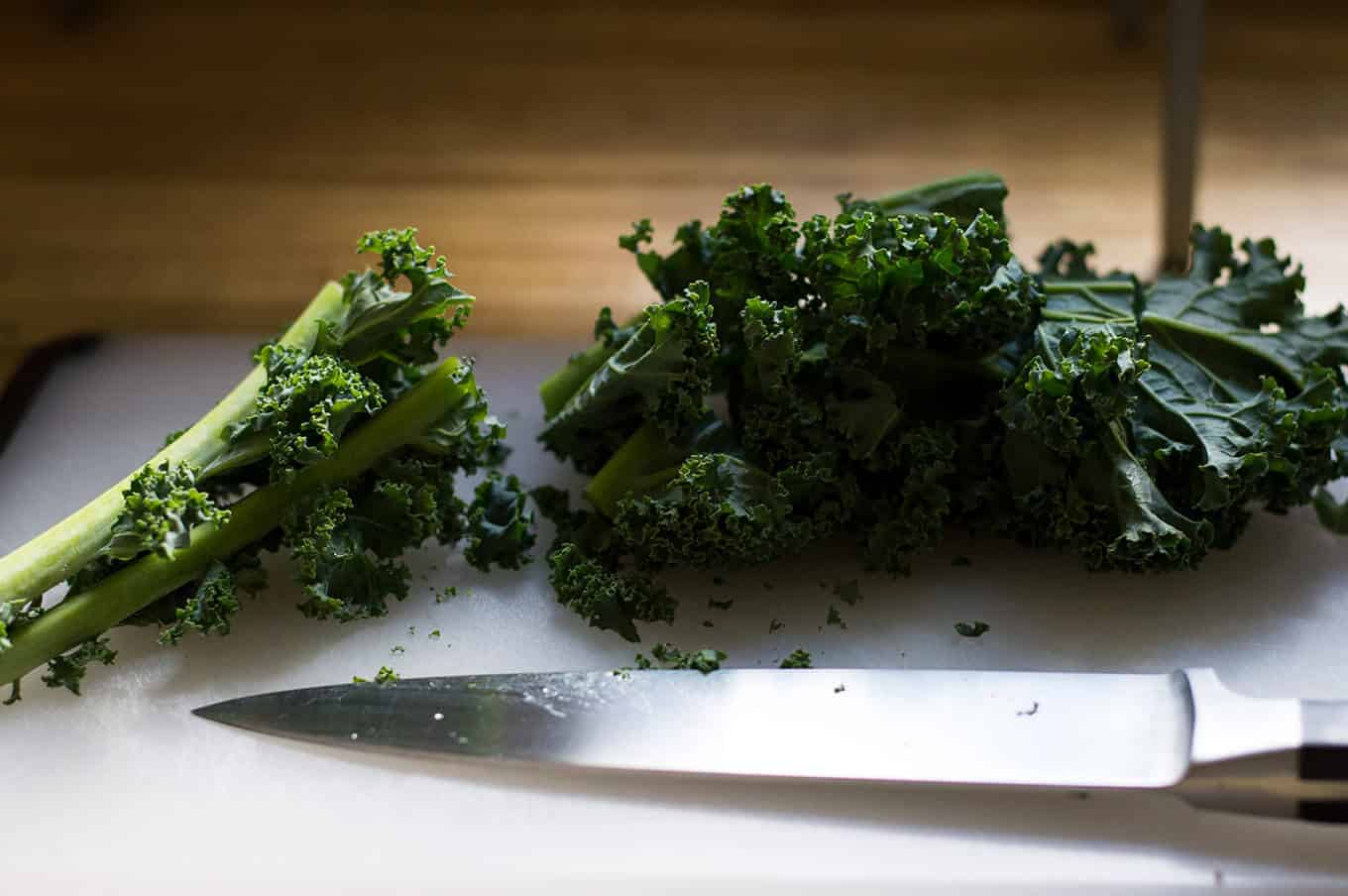 Chopped kale and chef\'s knife on a cutting board.