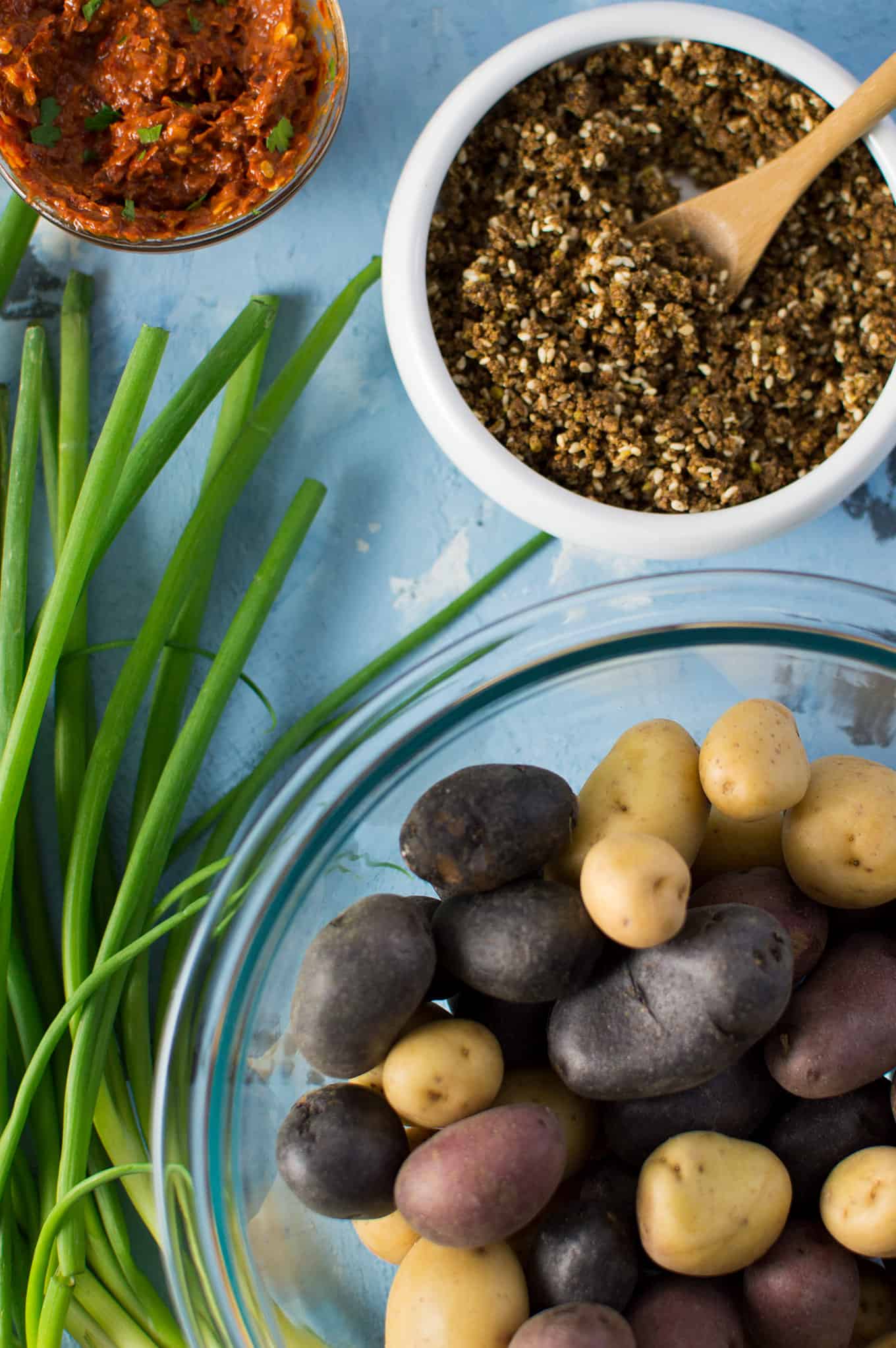 Scallions and bowls of fingerling potatoes, dukkah, and harissa on a  table.