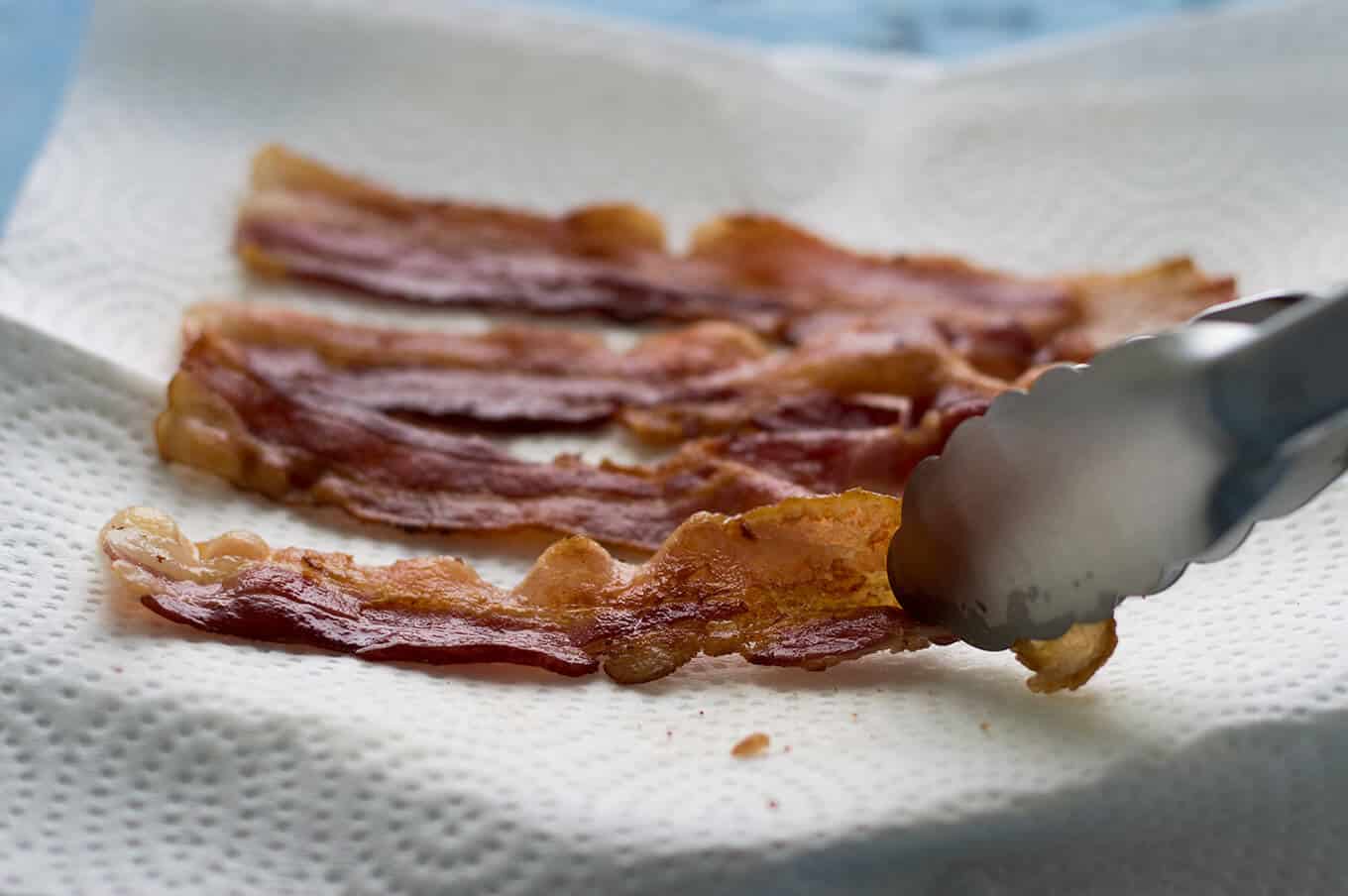 Slices of cooked bacon on a paper towel-lined plate.